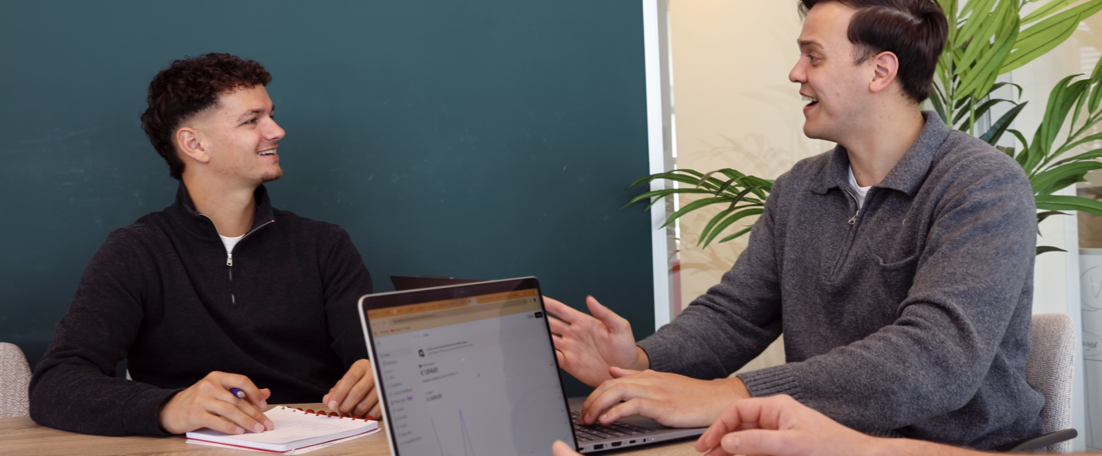 Twee collega's lachend in gesprek aan tafel